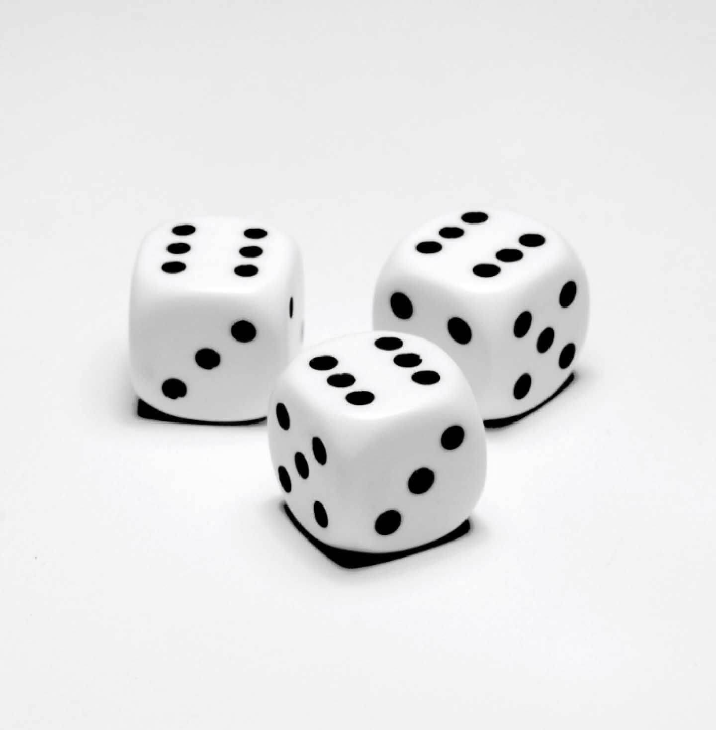 Foto di tre dadi da gioco bianchi e neri e girati sul numero sei. Sfondo grigio.