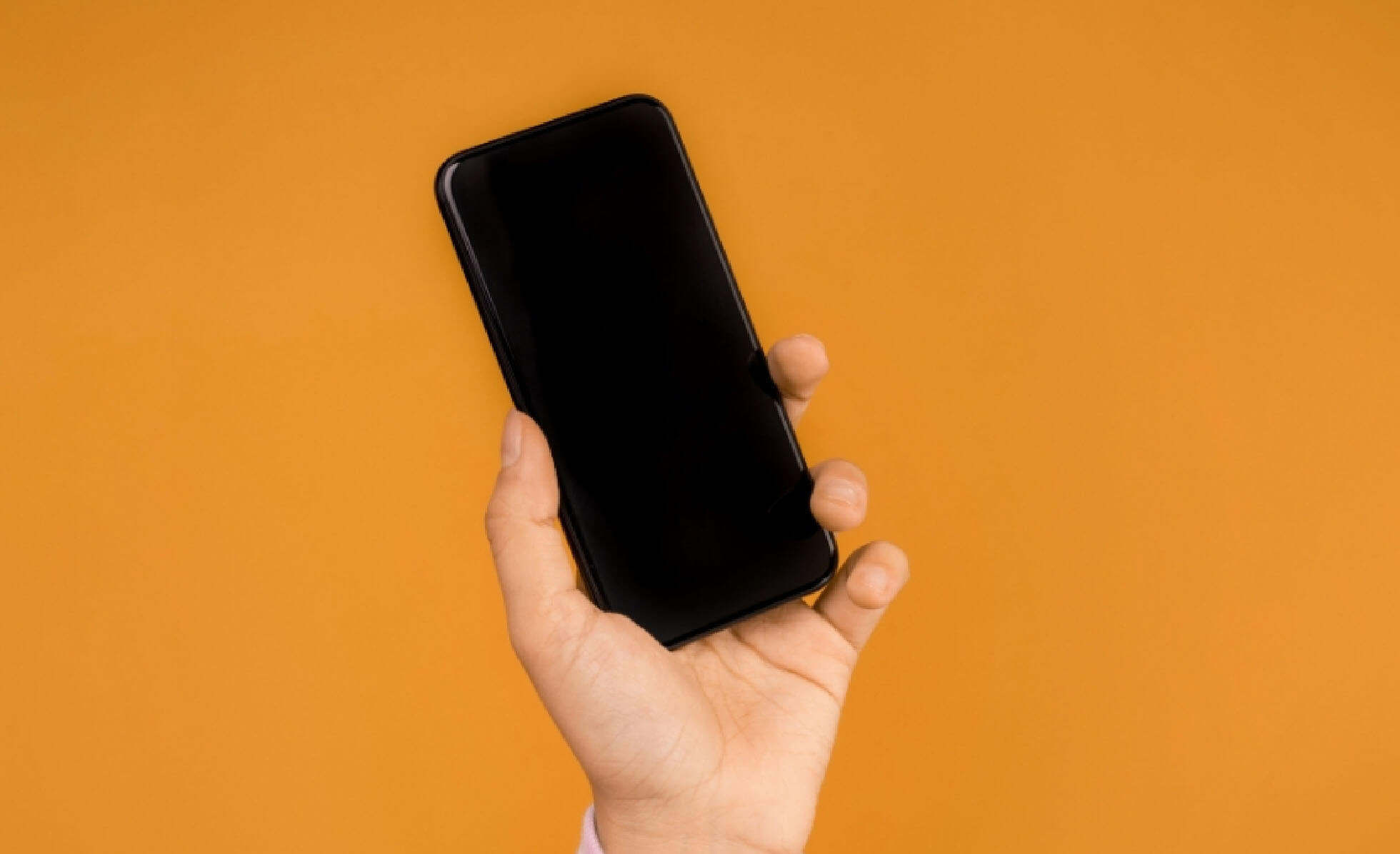 Foto di una mano che impugna uno smartphone su sfondo arancione.