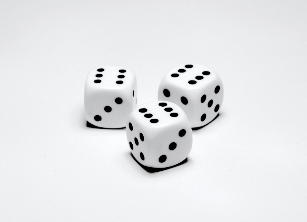 Foto di tre dadi da gioco bianchi e neri e girati sul numero sei. Sfondo grigio